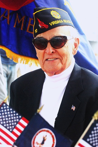 Staff Sgt Robert C. Melberg wearing his signature blue blazer, white turtle
                            neck sweater, sunglasses, and American Legion hat.