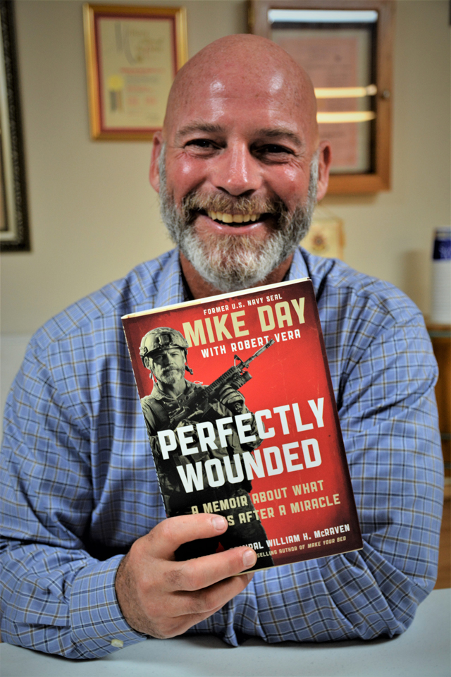 SCPO Mike Day, USN {Retired), a Navy Seal,                              holds a copy of his book 